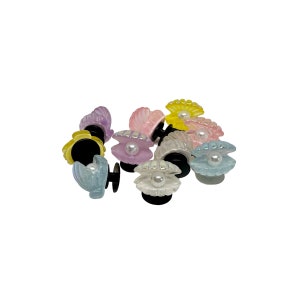May include: A group of ten pastel-colored plastic hair clips shaped like seashells with a pearl in the center. The shells are in various shades of pink, yellow, and blue.