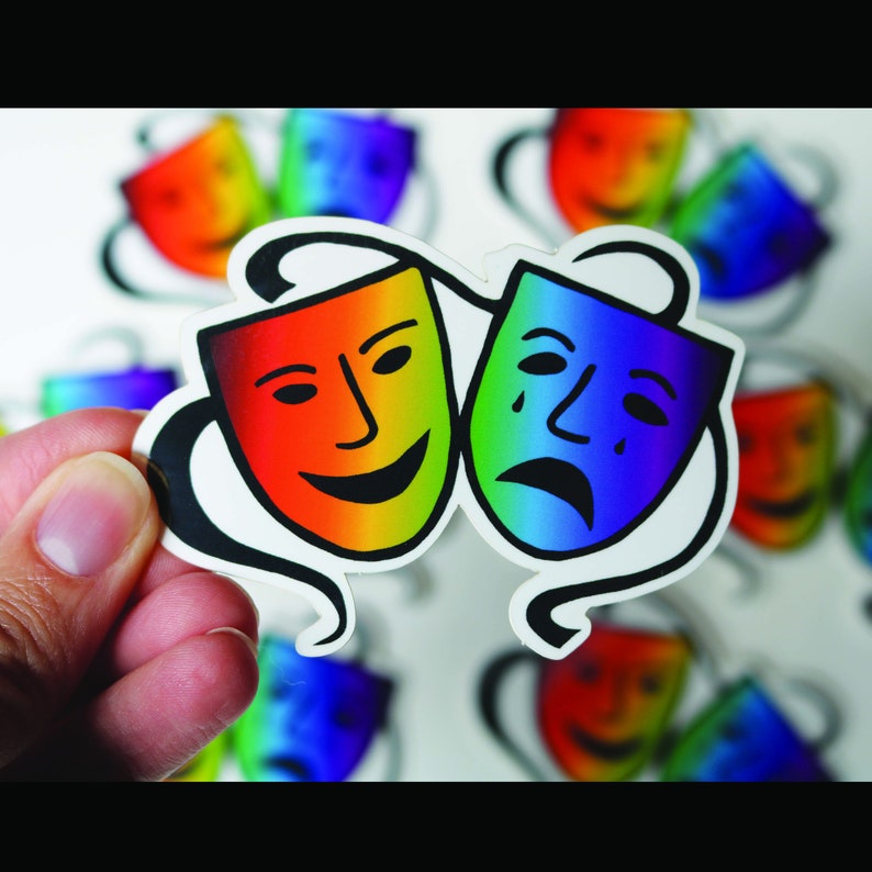 May include: A sticker featuring two theater masks: a smiling mask in rainbow colors and a sad mask in blue and green. The masks are connected by a black swirl design. Other masks are visible in the background.