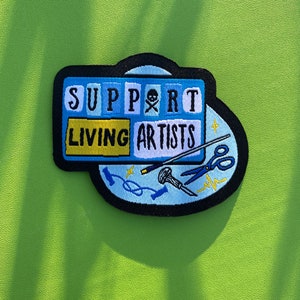 May include: A blue and yellow embroidered patch with the text "SUPPORT LIVING ARTISTS" and various art supplies, including a paintbrush, scissors, and thread.