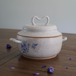 May include: White ceramic casserole dish with a lid and two handles. The dish has a speckled glaze and a blue floral design.