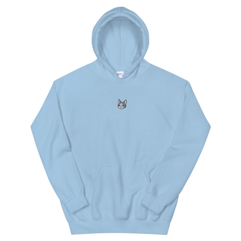 Op de afbeelding: Een lichtblauwe hoodie met een voorzak en een capuchon. De hoodie heeft een kleine geborduurde kattenkop op de borst. De kattenkop is grijs en wit met blauwe ogen. De hoodie is gemaakt van een zacht materiaal.