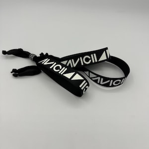 Puede incluir: Pulsera negra con la inscripción "AVICII" en blanco y un logotipo en forma de triángulo.