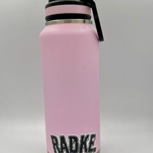 May include: A pink stainless steel water bottle with a black lid and a black sticker that says "RADKE" in dripping letters.