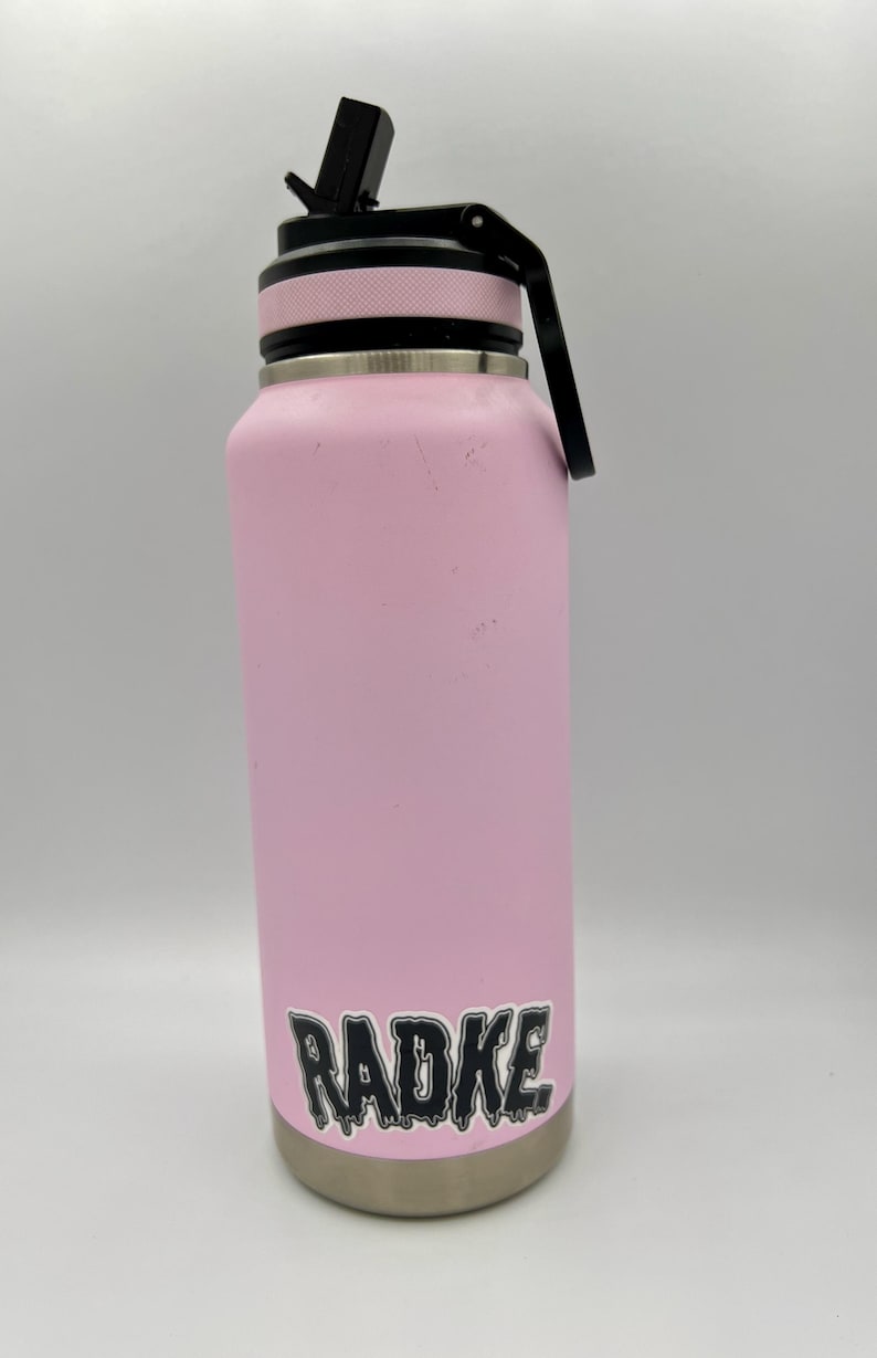 May include: A pink stainless steel water bottle with a black lid and a black sticker that says "RADKE" in dripping letters.