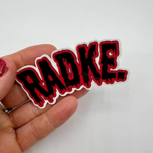 May include: A black and red sticker with the word "RADKE" written in a dripping, gothic font.