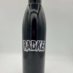 May include: Black stainless steel water bottle with a white sticker that says "RADKE" in dripping letters.