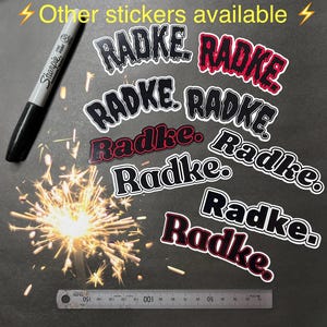 May include: A collection of black and red vinyl stickers with the word "Radke" written in a variety of styles. The stickers are arranged on a dark gray surface.