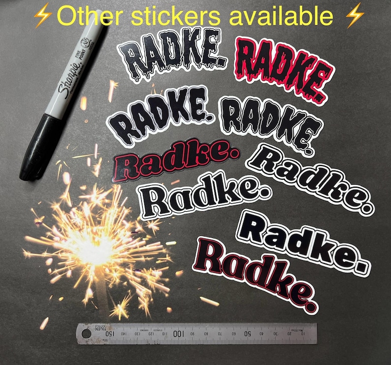 May include: A collection of black and red vinyl stickers with the word "Radke" written in a variety of styles. The stickers are arranged on a dark gray surface.