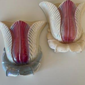 May include: Two ceramic wall-mounted flower vases. The vases are shaped like tulips, with iridescent white petals and a deep red centre. The base of the flower is a light blue colour.