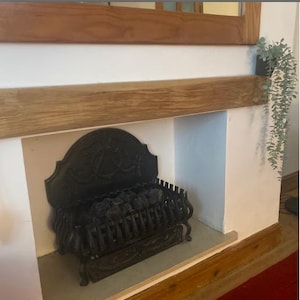 May include: A black cast iron fireplace insert with a decorative design and a grate for burning logs. The fireplace is set into a white wall with a wooden mantel above it.