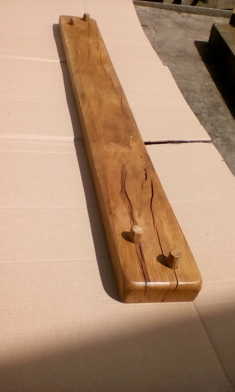 May include: A long, wooden shelf with three wooden pegs. The shelf is stained a light brown color and has a natural wood grain.