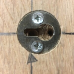 May include: Close-up of a metal keyhole cover with two screws. The cover is mounted on a wooden surface.