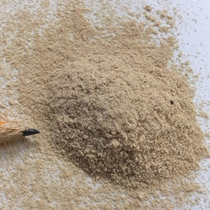 May include: A pile of light brown sawdust on a white surface. A pencil is visible in the bottom left corner of the image.