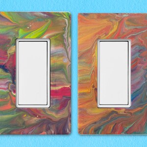 Könnte beinhalten: Zwei Lichtschalterabdeckungen mit einem farbenfrohen, abstrakten Marmormuster. Eine Abdeckung hat ein grünes, gelbes und rotes Marmormuster. Die andere Abdeckung hat ein gelbes, oranges und rotes Marmormuster.