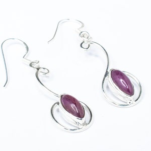 May include: A pair of silver earrings with a purple gemstone in each. The earrings have a delicate, curved design.