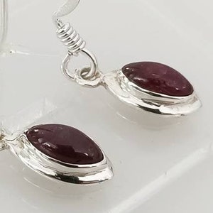 May include: A pair of silver earrings with maroon gemstone accents. The earrings have a simple, elegant design.