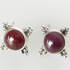 May include: A pair of silver earrings with a red gemstone in the centre of each earring. The earrings have a simple, geometric design.