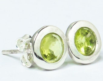 Puede incluir: Un par de pendientes de plata con piedras preciosas verdes. Los pendientes son redondos y tienen un diseño sencillo.