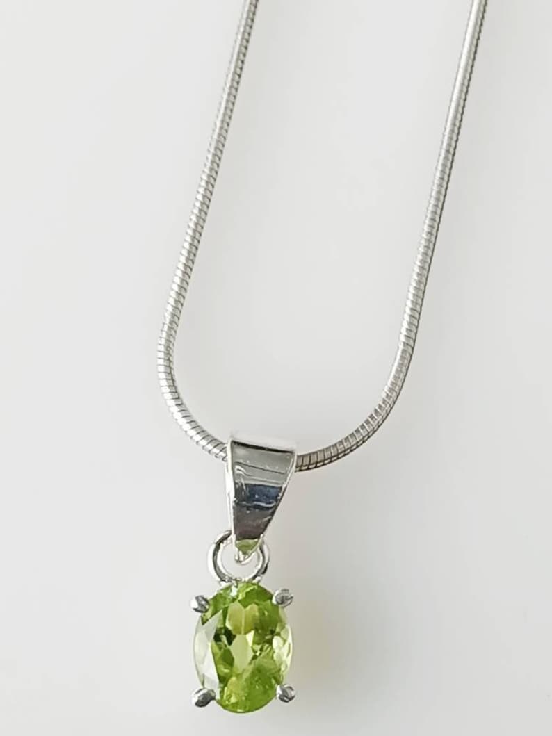 May include: A silver chain necklace with a pendant featuring a green oval peridot gemstone.