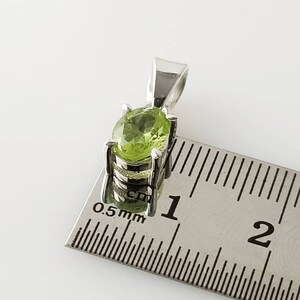 May include: A silver pendant with a green peridot gemstone. The pendant is approximately 1 cm in length.