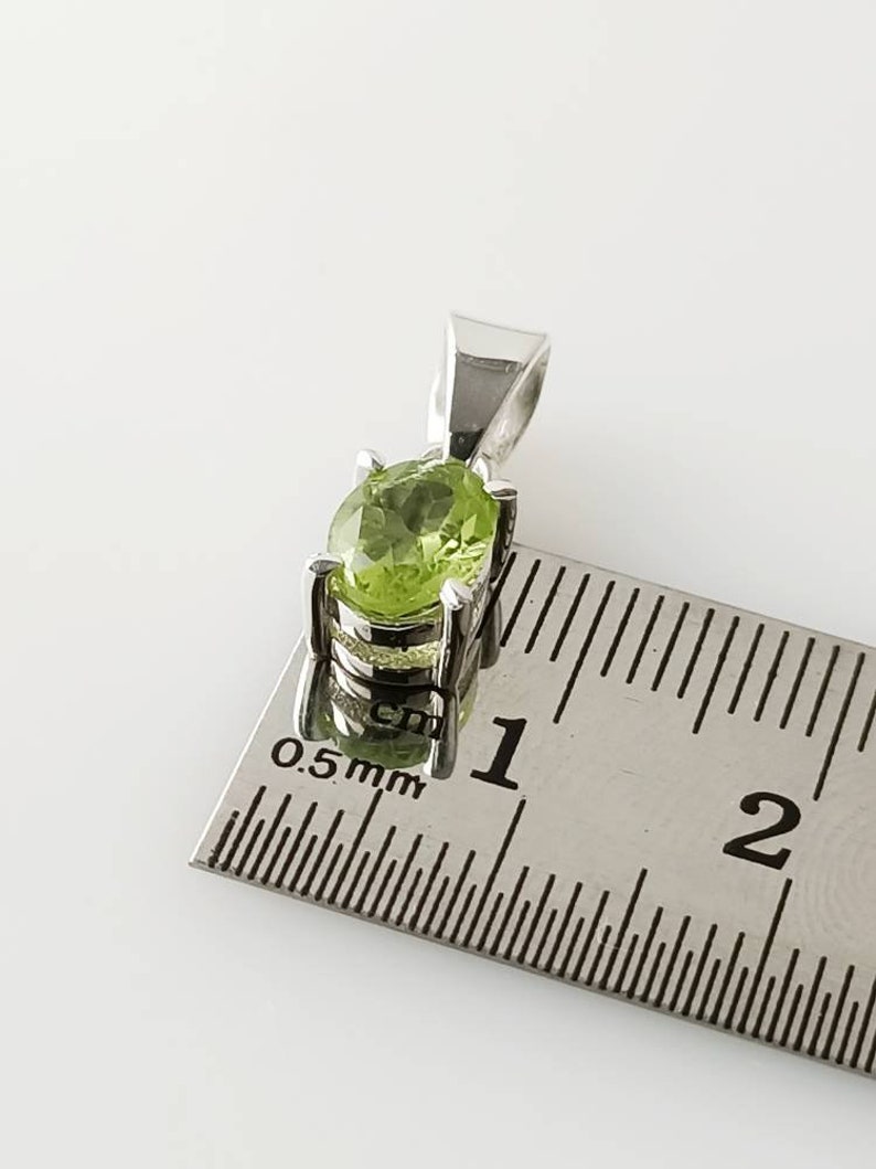 May include: A silver pendant with a green peridot gemstone. The pendant is approximately 1 cm in length.