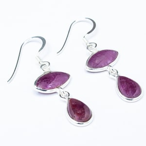 May include: A pair of silver dangle earrings with two pink gemstones on each earring. The top gemstone is oval shaped and the bottom gemstone is teardrop shaped.