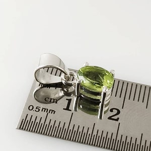 May include: A silver pendant with a green gemstone, measuring approximately 1 cm in diameter, is shown next to a ruler.