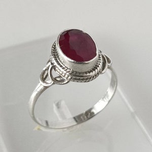 May include: A silver ring featuring a red oval gemstone set in an ornate bezel. The ring has a twisted band and a delicate design.