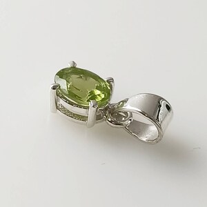 May include: A silver pendant with a green oval gemstone. The pendant has a simple design and is perfect for adding a touch of elegance to any outfit.