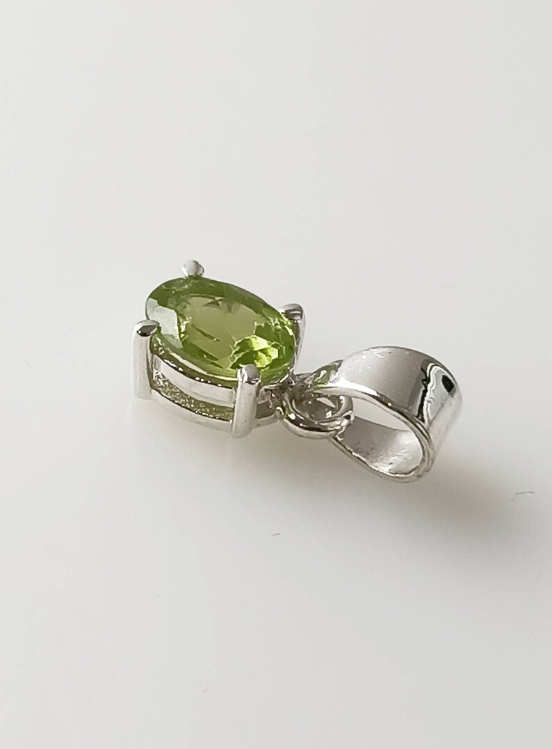 May include: A silver pendant with a green oval gemstone. The pendant has a simple design and is perfect for adding a touch of elegance to any outfit.