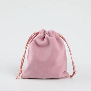 May include: A pink velvet drawstring pouch with a gathered top and a cord closure. The pouch is made of soft, plush velvet and is perfect for storing small items.