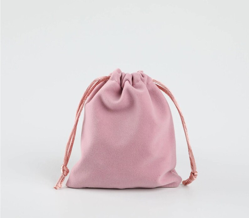 May include: A pink velvet drawstring pouch with a gathered top and a cord closure. The pouch is made of soft, plush velvet and is perfect for storing small items.