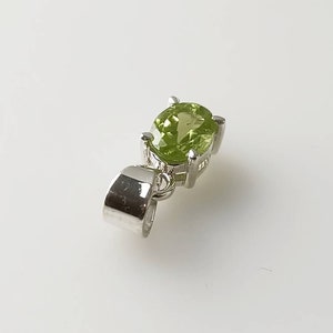 May include: A silver pendant with a green gemstone. The pendant has a bail for attaching to a chain.