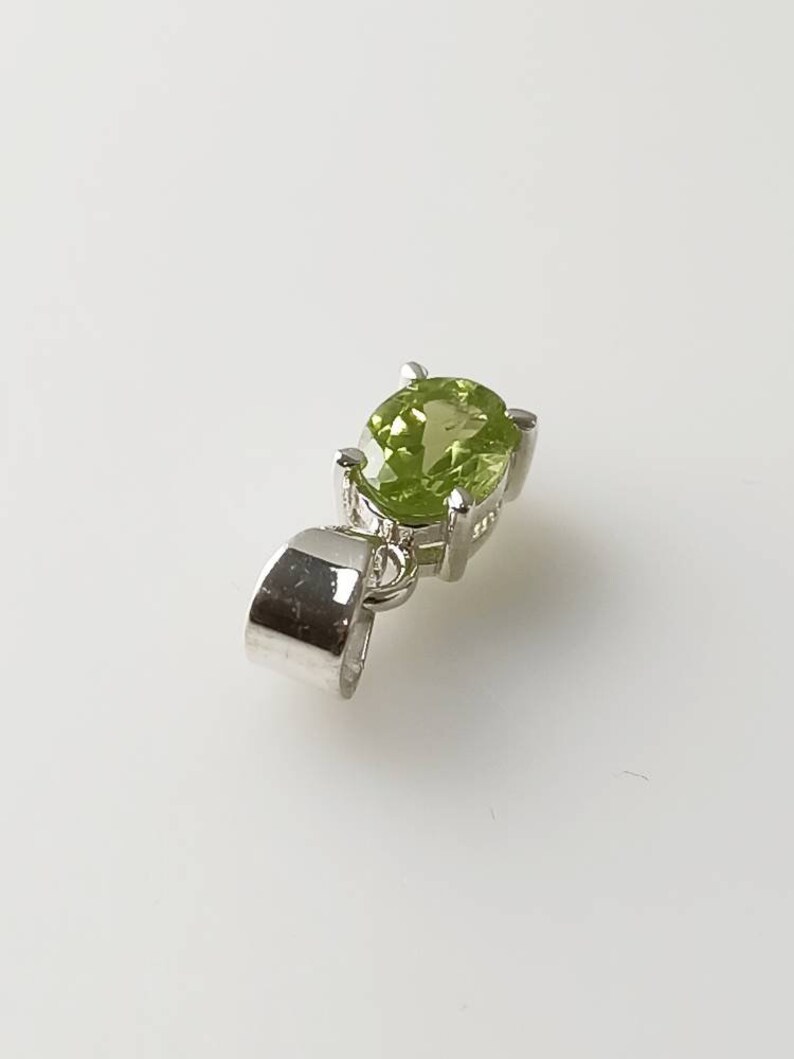 May include: A silver pendant with a green gemstone. The pendant has a bail for attaching to a chain.