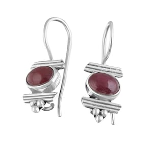 Könnte beinhalten: Ein Paar silberne Ohrhänger mit einem maroonfarbenen Edelstein in der Mitte jedes Ohrrings. Die Ohrringe haben ein geometrisches Design mit drei horizontalen Balken und einem Cluster aus drei silbernen Perlen am unteren Ende.