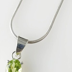 May include: A silver chain necklace with a pendant featuring a green oval peridot gemstone.