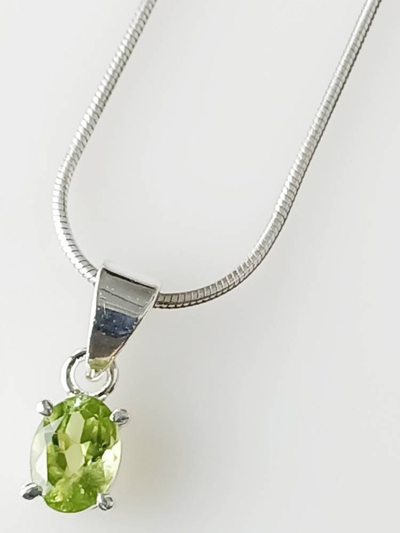 May include: A silver chain necklace with a pendant featuring a green oval peridot gemstone.