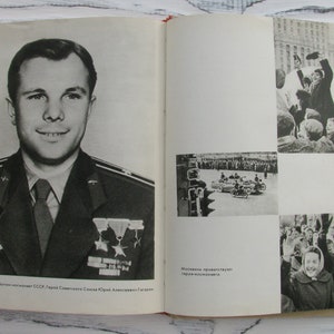 May include: A vintage book open to a black and white photograph of a man in a military uniform, with medals. The opposite page shows additional black and white images of a crowd and vehicles. Text is present in the image.