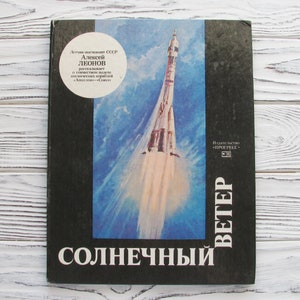 May include: A vintage book with a black cover featuring a vibrant illustration of a rocket launching into space against a blue sky. The title "SOLNECHNY" is prominently displayed, with additional text in Russian. The book is a retro space exploration theme.