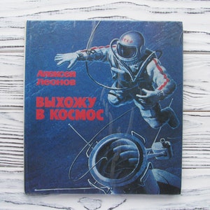 May include: A vintage book cover featuring an astronaut in a spacesuit against a dark blue background. The astronaut is depicted floating in space, with the text "Алексей Леонов ВЫХОЖУ В КОСМОС" in red and yellow. The cover has a retro, space exploration theme.