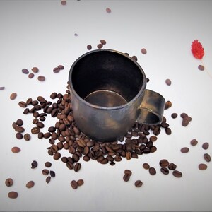 May include: A dark brown ceramic coffee mug with a handle, surrounded by coffee beans on a white background.