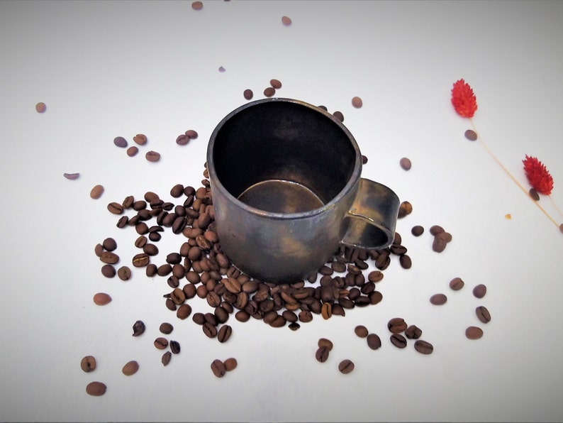 May include: A dark brown ceramic coffee mug with a handle, surrounded by coffee beans on a white background.