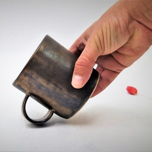 May include: A dark brown ceramic mug with a handle. The mug has a rustic, hand-thrown look.