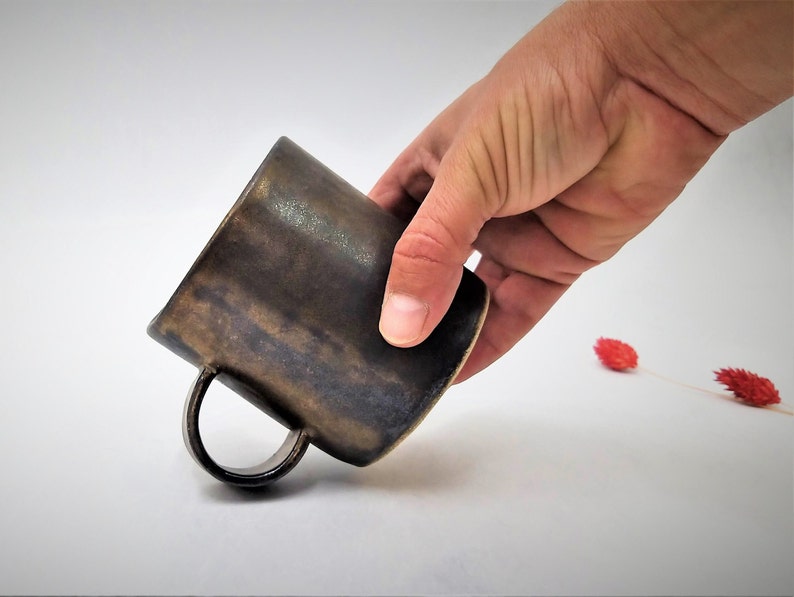 May include: A dark brown ceramic mug with a handle. The mug has a rustic, hand-thrown look.