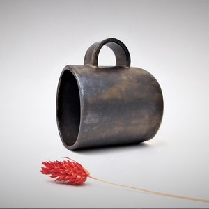 May include: A dark brown ceramic mug with a rounded handle. The mug has a rustic, textured finish.