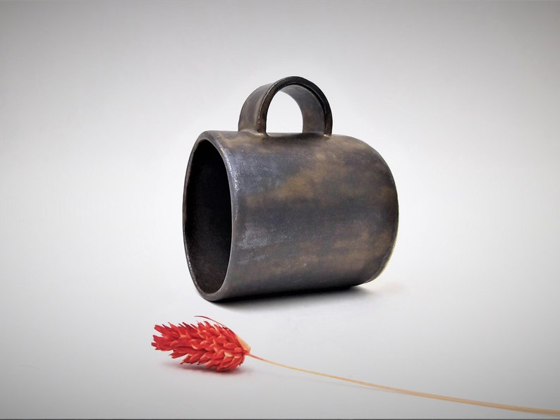 May include: A dark brown ceramic mug with a rounded handle. The mug has a rustic, textured finish.