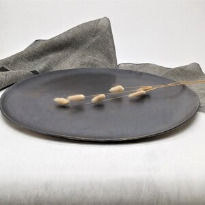 May include: A dark gray ceramic serving platter with a smooth, slightly textured surface. A sprig of dried, light brown grasses is placed on the platter.