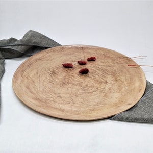 May include: A large, round, wooden serving tray with a natural wood finish. The tray has a slightly rough texture and is decorated with small, red dried flowers.