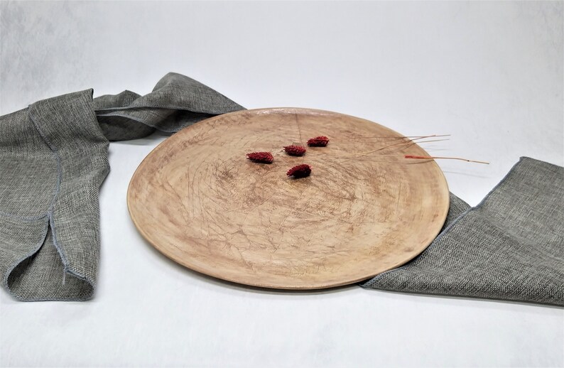 May include: A large, round, wooden serving tray with a natural wood finish. The tray has a slightly rough texture and is decorated with small, red dried flowers.