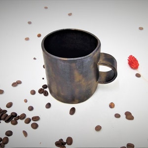 May include: A dark brown ceramic coffee mug with a textured, speckled finish. The mug has a rounded handle and a wide, slightly flared rim.